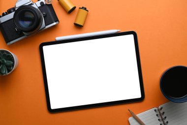 Portakal rengi arka planda dijital tablet, kamera ve not defteri olan fotoğrafçı iş yerinin genel görüntüsü..