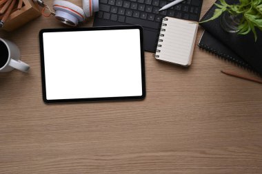 Beyaz ekran, not defteri, klavye, kulaklık ve tahta masadaki kopyalama alanı ile dijital tabletin üst görünümü.