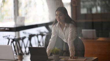 Kendine güvenen genç bayan ofis çalışanı ofiste dikiliyor ve başka tarafa bakıyor..