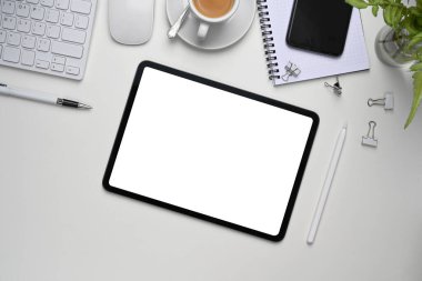 Dijital tablet, akıllı telefon ve ofis malzemeleriyle beyaz ofis masasının üst görüntüsü.