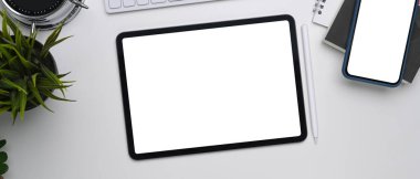 Beyaz masadaki boş ekran ile dijital tabletin ve akıllı telefonun üst görünümü.