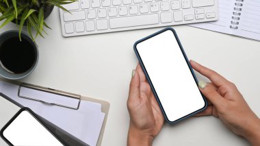 Beyaz ofis masasında boş ekranlı cep telefonu tutan genç bir kadın..