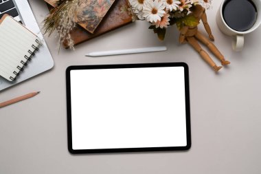 Boş ekranlı dijital tabletin üst görünümü, stilus kalem, not defteri ve beyaz masadaki kahve fincanı.