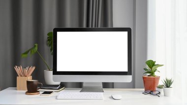 Boş ekran, ev bitkisi ve ofis malzemeleri beyaz ofis masasında olan bilgisayarın ön görüntüsü.