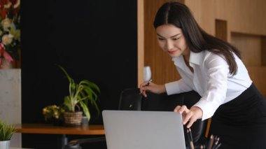 Modern ofiste gülümseyen ve bilgisayarla çalışan çekici bir iş kadını..