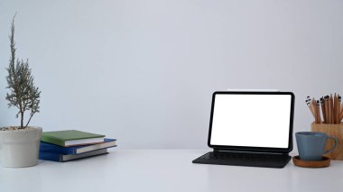 Bilgisayar tableti, ev bitkisi, kitaplar, kahve fincanı ve kalem tutacağı tasarımcı işyerinde.