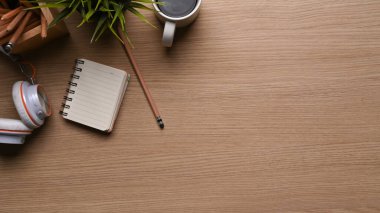 Kahve fincanı, kulaklık, bitki, defter ve tahta arka planda fotokopi alanı olan ofis masasının üst görüntüsü.