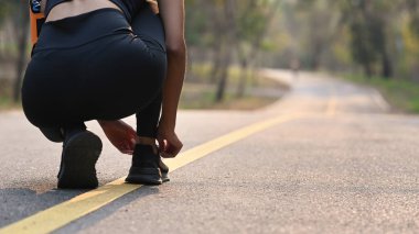 Ayakkabı bağcıkları bağlayan genç bir kadın parkta koşuya hazırlanıyor..