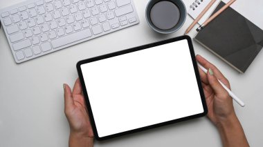 Beyaz masa üzerinde dijital tablet ve stil kalem tutan kadın elleri.