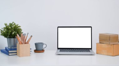 Boş ekran, ev bitkisi, kalem tutacağı ve beyaz masadaki kutularla bilgisayar dizüstü bilgisayarının ön görüntüsü.