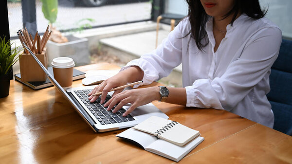 Cropped shot of businesswoman hands typing on computer laptop at office desk.