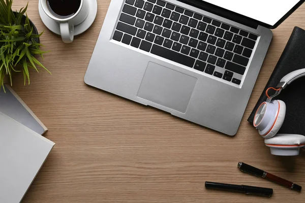 Bilgisayarı, kulaklığı, kahve fincanını, defterini, kalemlerini ve bitkilerini ahşap masaya yerleştirme görüntüsü.