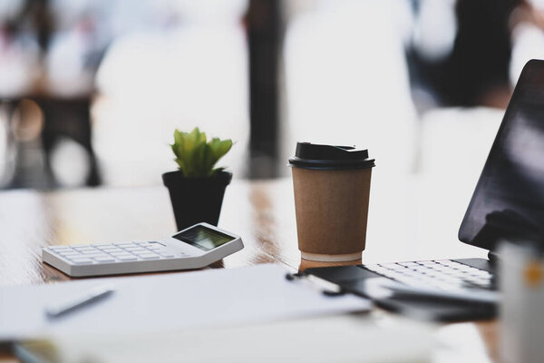 Бухгалтер на рабочем месте с кофейной чашкой, ноутбуком, калькулятором и документами на деревянном столе.