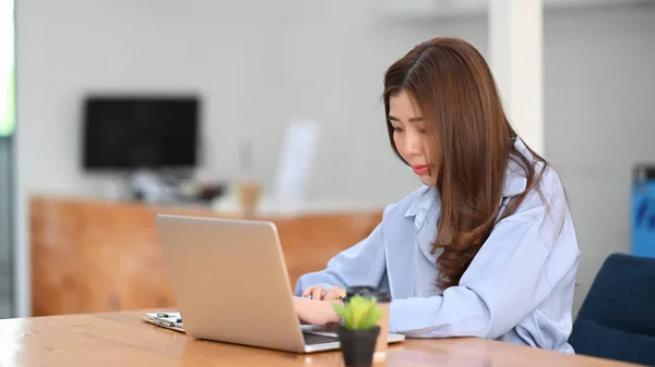 女性のオフィスワーカーはオフィスのデスクでラップトップコンピュータに集中して作業する — ストック写真