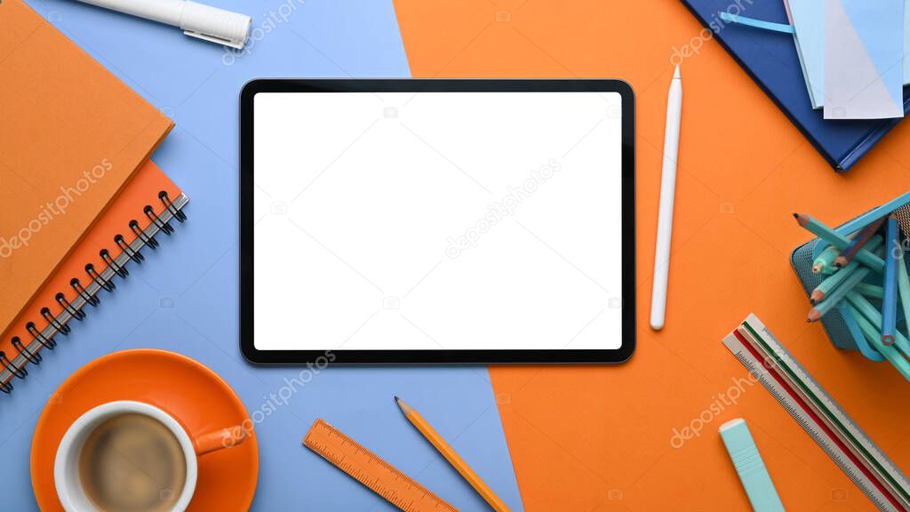 Top view of creative designer workplace with digital tablet and office supplies on two tone blue and orange background.