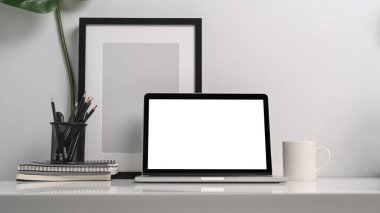 Bilgisayarı, kalem tutacağı, siyah boş fotoğraf çerçevesi ve beyaz masada kahve fincanı olan minimum iş yeri.