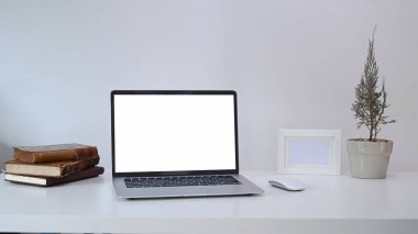 Bilgisayar dizüstü bilgisayarı, tesisi, boş fream ve beyaz masadaki kitapları olan tasarımcı işyeri.