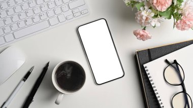 Boş ekranlı akıllı telefon, kahve fincanı ve ofis malzemelerini beyaz ofis masasına koyun..