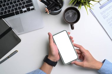 Beyaz ofis masasında boş ekranlı cep telefonu tutan bir iş adamı..