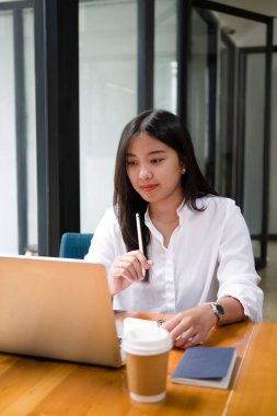 Modern ofiste oturan ve ekran bilgisayarına bakan düşünceli genç bir kadın..