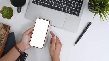 Akıllı telefonu tutan ve beyaz masaya boş ekranlı yazı yazan kadının üst görüntüsü