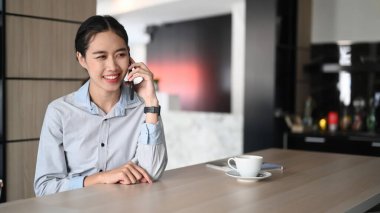 Modern ofiste oturan ve cep telefonuyla konuşan mutlu genç iş kadını..