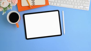 Boş ekran, kahve fincanı, not defteri ve mavi arkaplanda stil kalemi ile dijital tableti taklit et.