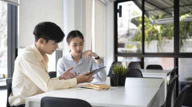 Finans raporunu analiz eden ve modern ofiste dizüstü bilgisayarla çalışan iki genç iş adamı..