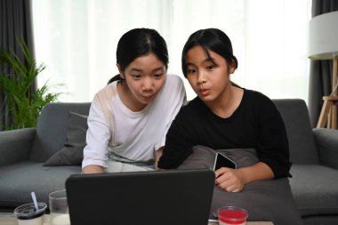 Two asian girl sitting on sofa and watching online cartoons with digital tablet at home.