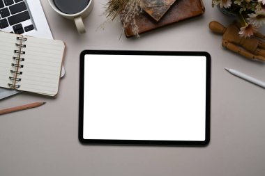 Dijital tableti, bilgisayarı, kahve fincanı ve defteri olan beyaz ofis masasının üst görüntüsü.