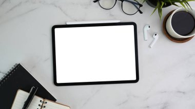 Dijital tablet, defter, kahve fincanı ve mermer arka planda kablosuz kulaklıkla çalışan tasarımcı çalışma masasının üstünde.