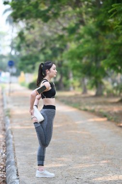 Sporcu kadının dışarıda antremandan önce bacaklarını esnetirken yan görünümü.