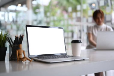 Beyaz ofis masasında boş ekranı olan ve arka planda oturan iş kadını bilgisayarını kapat.