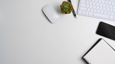 Beyaz ofis masasının üstünde boş defter, akıllı telefon, klavye, kaktüs ve kopyalama alanı.