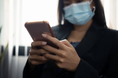 Ofiste cep telefonu kullanan koruyucu maskeli bir iş kadını görüntüsü..