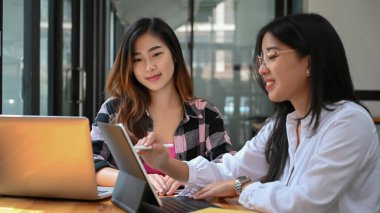 İki genç tasarımcı yeni bir başlangıç projesi üzerinde çalışıyor ve yaratıcı ofiste bilgisayar tableti kullanıyor.