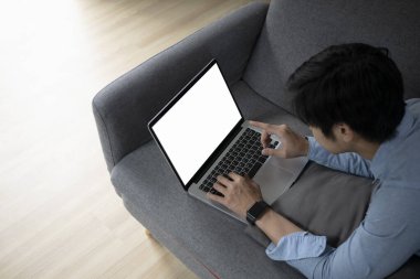 Genç adam kanepede uzanıyor ve evdeki dizüstü bilgisayarda internette sörf yapıyor..