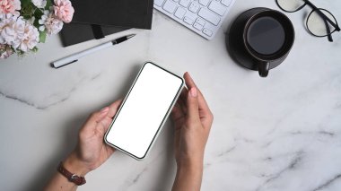 Kadın ellerinin üst görüntüsü mermer masada beyaz ekranlı akıllı telefonu taklit ediyor..