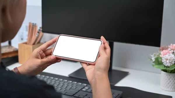 Close up over shoulder view of woman hands holding horizontal mobile phone with blank screen.