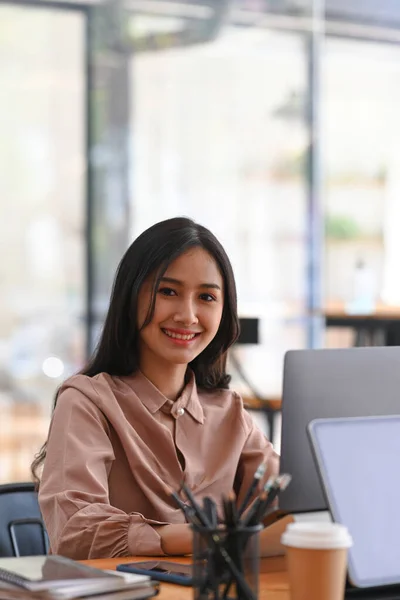 職場に座ってカメラに微笑む幸せな若い女性従業員の肖像 — ストック写真