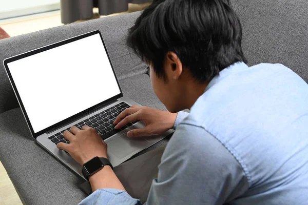 自宅で快適なソファに横たわって コンピュータのラップトップでオンラインで作業しているカジュアルなアジア人男性 — ストック写真