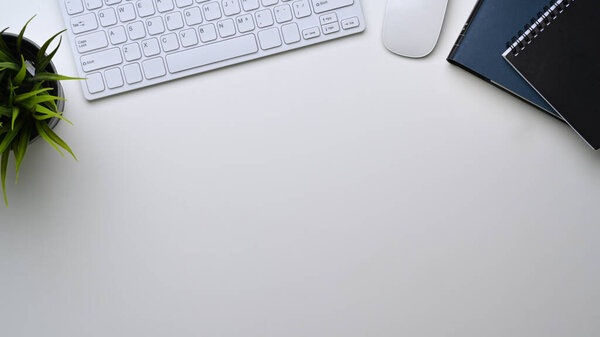 Top view of white offie desk with wireless keybord, house plant, notebook ad copy space.