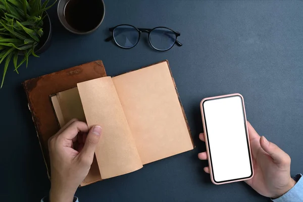 Woman hands holding mock up smart phone and opening notebook on black leather.