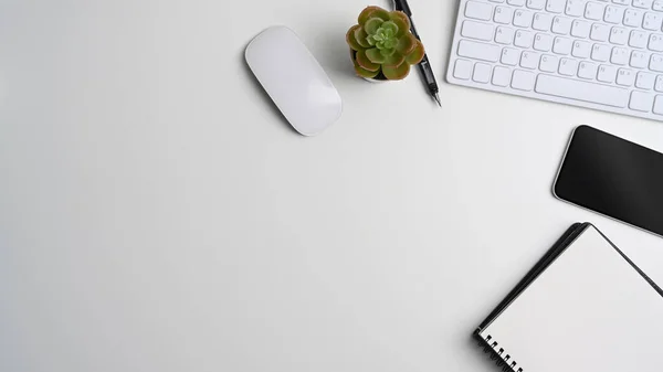 Above view of white office desk with empty notebook, smart phone, keyboard, cactus and copy space.