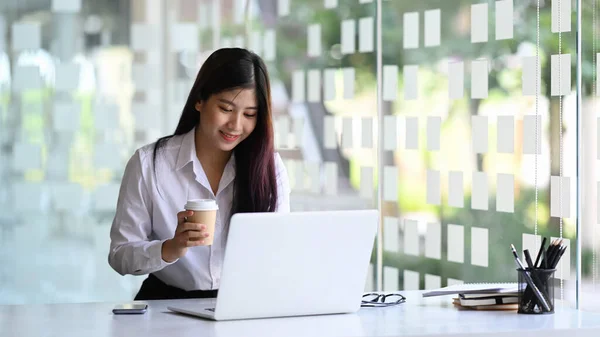 幸せな若いアジアの女性のオフィスワーカーは コーヒーカップを保持し ラップトップコンピュータ上で作業 — ストック写真