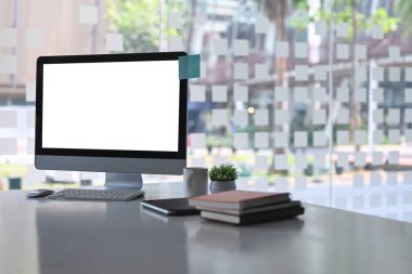 Bilgisayarı, kitapları, kahve fincanı ve bitkisi olan modern ofis beyaz ofis masasında..