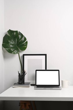Bilgisayar dizüstü bilgisayarı, kalem tutacağı, kahve fincanı, defter ve boş fotoğraf çerçevesiyle modern işyerinin ön görüntüsü.