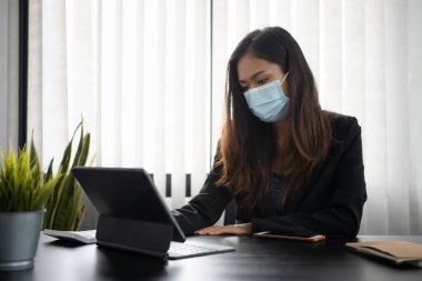 Koruyucu maskeli iş kadını, iş yerindeki bilgisayar tabletine odaklan.