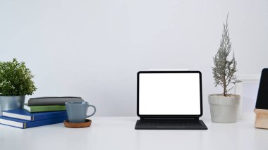 Beyaz masa üzerinde bilgisayar tableti, bitki, kitap ve kahve fincanı olan modern işyeri.