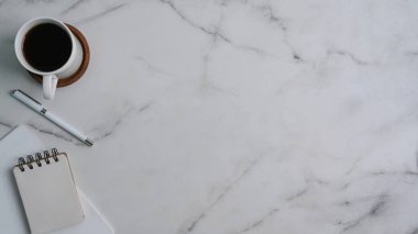 Kahve fincanı, boş defter, mermer zemin üzerinde kalem ve kopya alanı ile modern çalışma alanının üst görünümü.